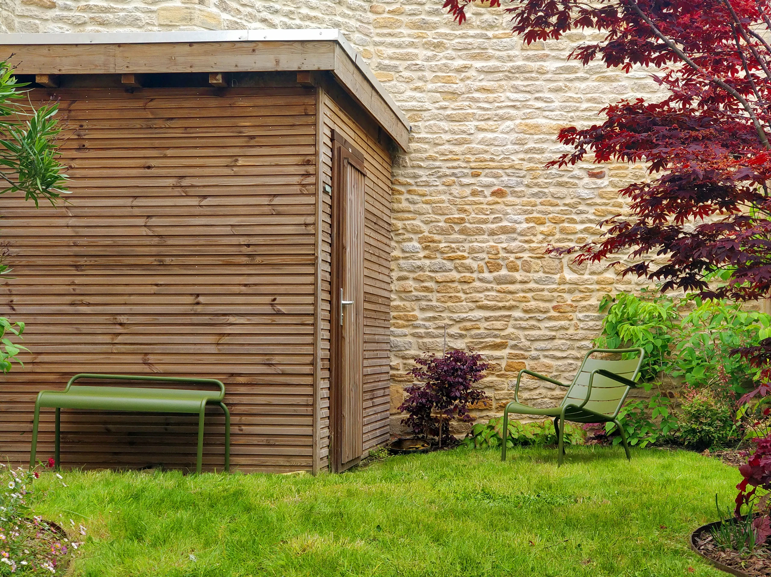 Abri de jardin en bardage bois horizontal contre un mur en pierre, avec salon de jardin vert, réalisé à Noyon — Colver