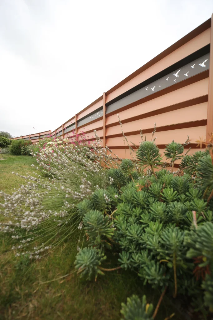 Brise-vue à lames aluminium teinte terracotta avec massif de vivaces et gazon — Colver paysagiste