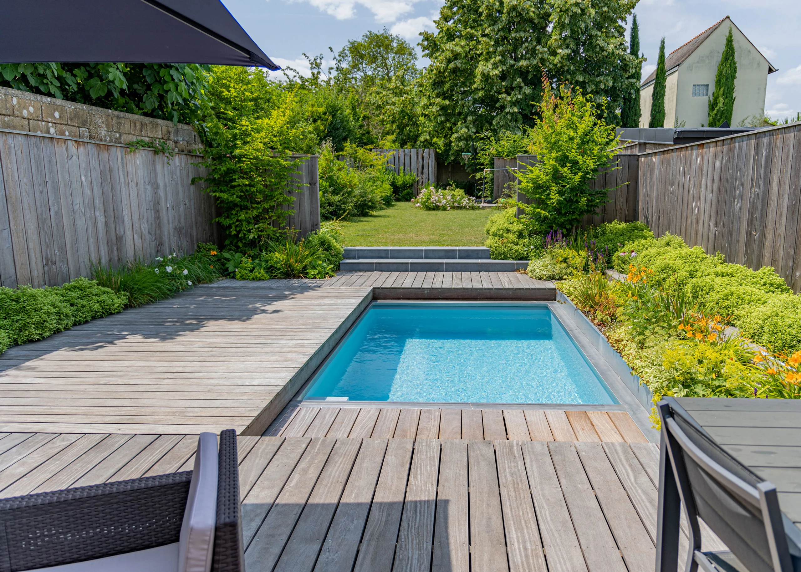 Piscine rectangulaire avec plage en bois thermofrêne et massifs fleuris dans un jardin — Saint-Quentin, Aisne — Colver