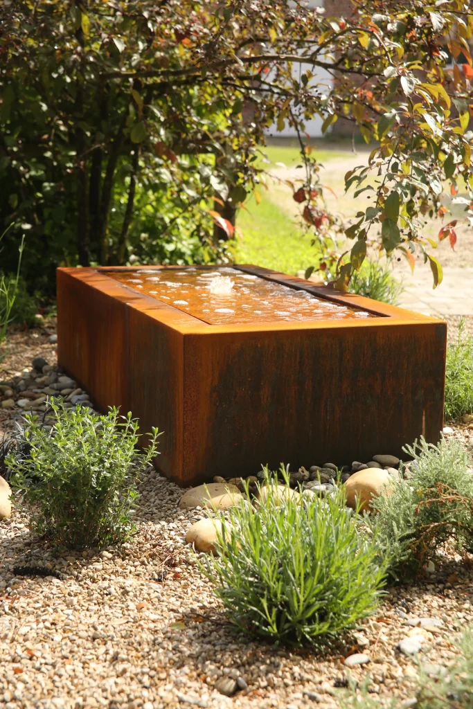 Fontaine miroir en acier Corten intégrée dans un massif de vivaces sur gravier — création Colver Oise