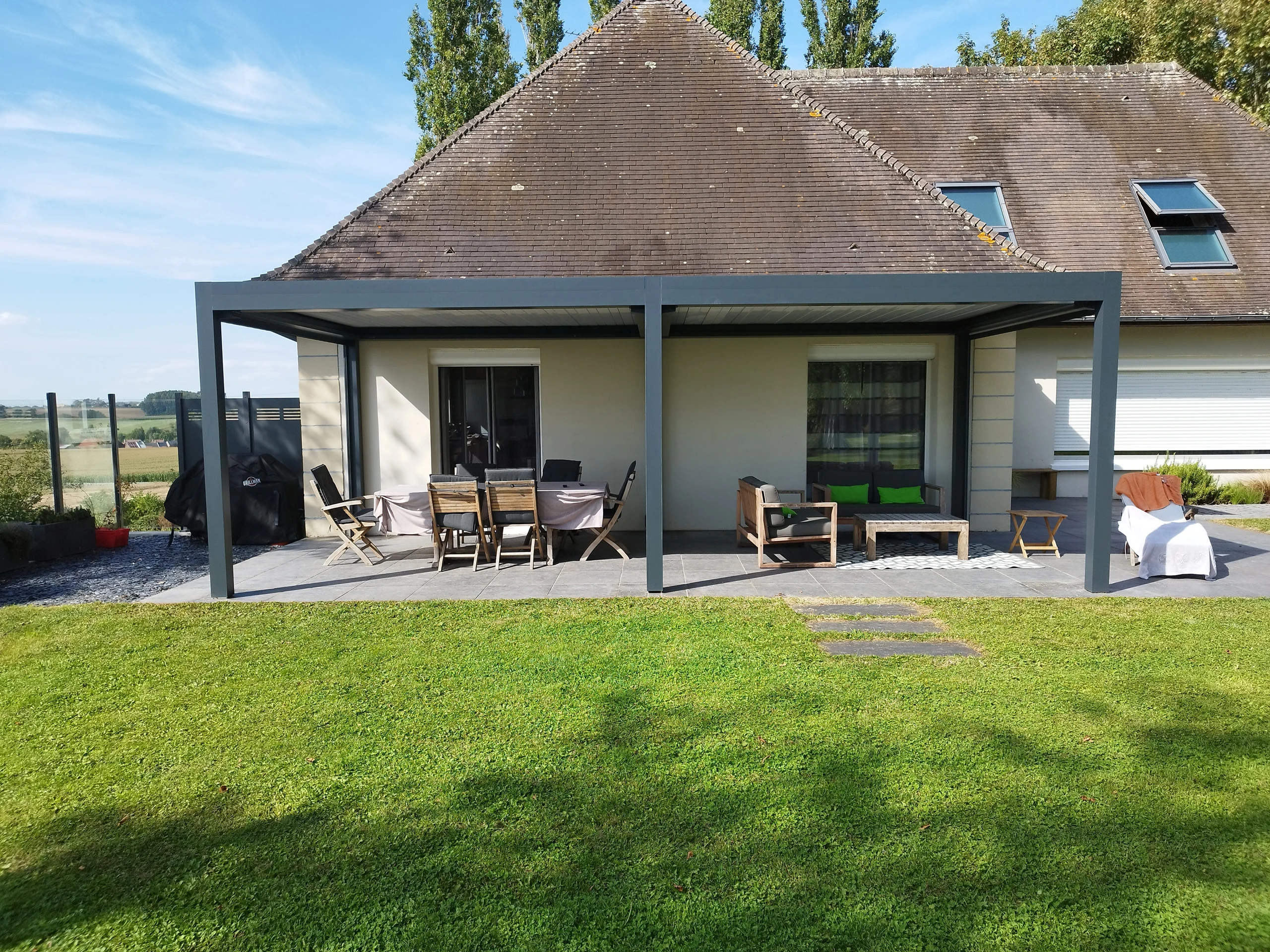Pergola aluminium bioclimatique adossée à une maison avec terrasse en dallage et salon extérieur à Saint-Quentin — Colver