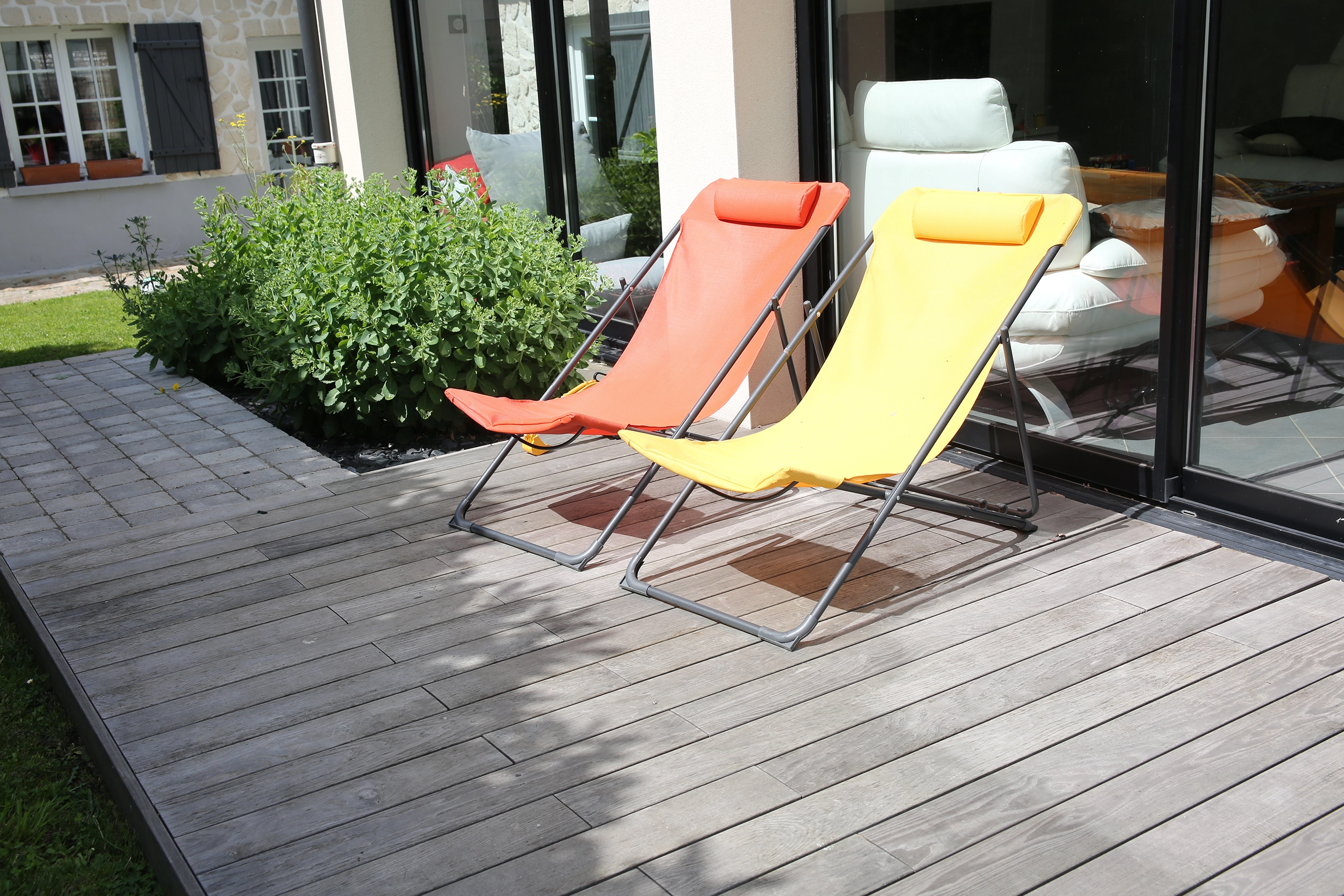 Terrasse en bois composite gris avec deux transats colorés orange et jaune devant baie vitrée — Compiègne, Oise — Colver