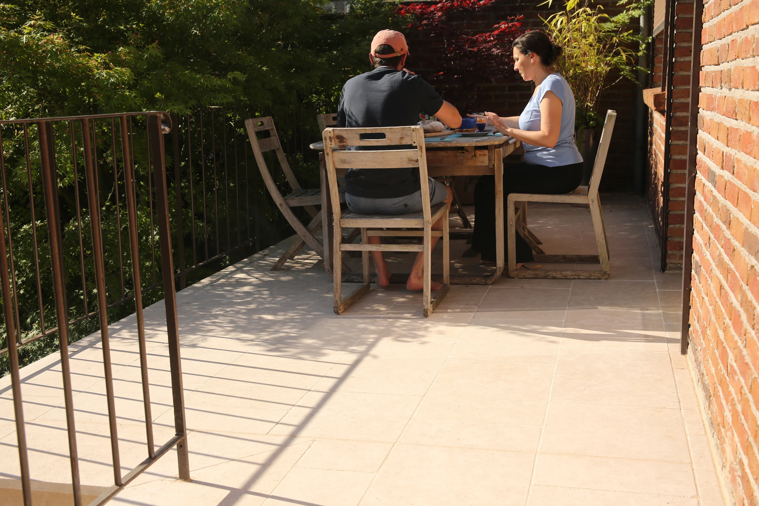 Couple prenant un repas sur terrasse carrelée travertin avec garde-corps métal et vue sur jardin arboré — Noyon, Oise — Colver